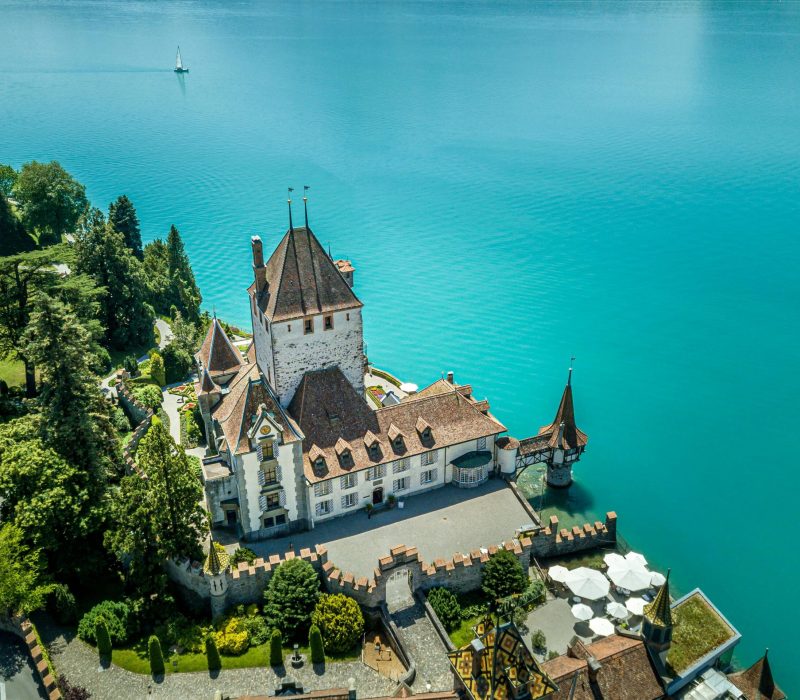 A stunning aerial view of Oberhofen Castle on the shores of Lake Thunersee in Switzerland, surrounded by turquoise waters.